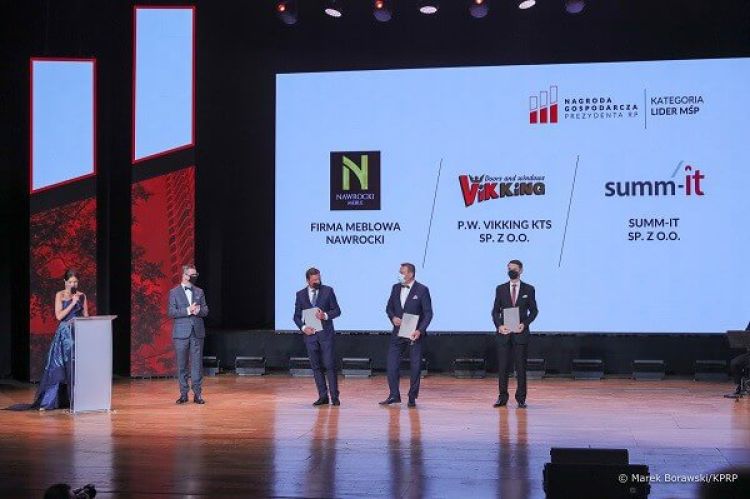 Mężczyźni stojący na scenie z nagrodami